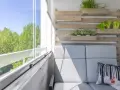 Przytulny balkon z szarą sofą, poduszką z liskiem i zielenią. Idealne miejsce, by zastanowić się, co na balkon posadzić.