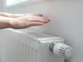 Dłonie ogrzewają się nad grzejnikiem, kiedy grzeją w blokach. Ciepło rozchodzi się po pokoju.