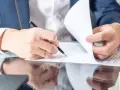 Mężczyzna w garniturze podpisuje dokumenty, co może oznaczać przedłużenie umowy najmu okazjonalnego.