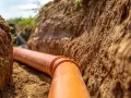 Pomarańczowa rura kanalizacyjna w wykopie. Może być podstawą do ubiegania się o odszkodowanie za studzienki na działce.