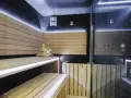 Nowoczesna sauna w domu z drewnianymi ławami, kamiennym piecem i dyskretnym oświetleniem LED. Idealne miejsce na relaks.