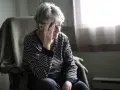 Zmartwiona starsza kobieta w paski, myśląca o pobycie w DPS, gdy ma mieszkanie własnościowe.