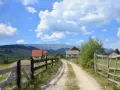 Droga wiejska z drewnianym płotem, domami i górami w tle. Współwłaściciel drogi nie wyraża zgody na jej dalsze użytkowanie.