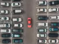 Widok z góry na parking, gdzie samochody są zaparkowane w strefie zamieszkania. W centrum wyróżnia się czerwony samochód.