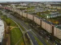 Najdłuższy blok w Polsce, falujący budynek mieszkalny z pomarańczową elewacją, otoczony zielenią i drogą z samochodami.