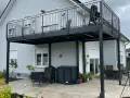Nowoczesne balkony dostawne na słupach, z czarną balustradą, dodają uroku domowi. Sprawdź, jaka cena za takie rozwiązanie.