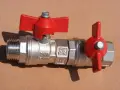 Metalowy zawór kulowy z czerwonymi rączkami, kluczowy element instalacji wodnej, stanowiący główny zawór wody w mieszkaniu.