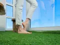 Bose stopy na sztucznej trawie na balkonie, w tle okno z odbiciem nieba. Nawet gdy pada deszcz, balkon z zieloną trawą wygląda jak oaza.
