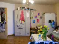 Przytulne mieszkanie dla samotnej matki. Szafa, piec kaflowy, kanapa, stolik z tulipanami i dziecięce rysunki na ścianie tworzą domową atmosferę.