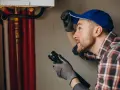 Instalator z latarką bada rury. Sąsiad nie zgadza się na wymianę pionu, co utrudnia pracę.