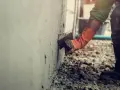 Pracownik w pomarańczowych rękawicach tynkuje ścianę. Brak zgody sąsiada na ocieplenie budynku opóźnia prace.