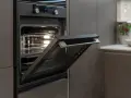 Nowoczesny piekarnik do zabudowy z uchylonymi drzwiczkami, wbudowany w szarą zabudowę kuchenną.
