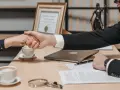 Uścisk dłoni prawnika i klienta. Na biurku dokumenty, kawa i laptop. Czy można cofnąć darowiznę mieszkania?