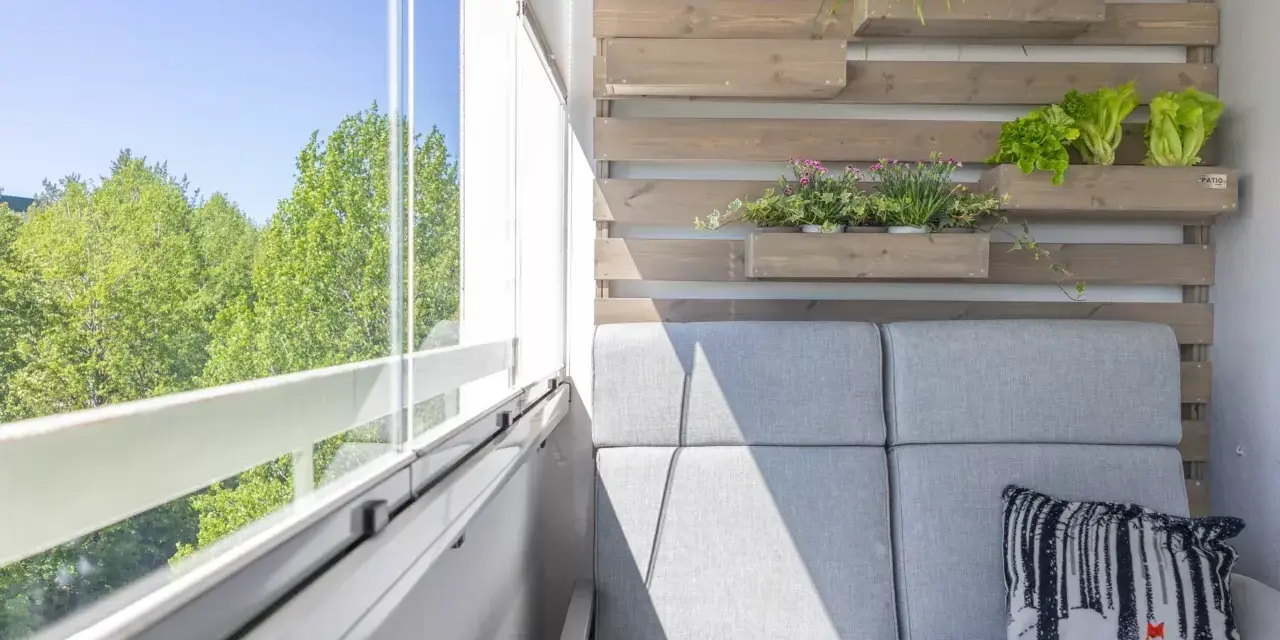 Przytulny balkon z szarą sofą, poduszką z liskiem i zielenią. Idealne miejsce, by zastanowić się, co na balkon posadzić.