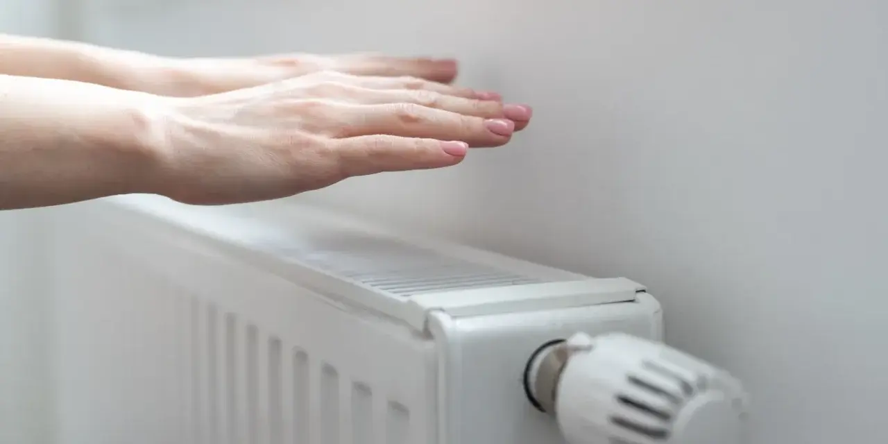 Dłonie ogrzewają się nad grzejnikiem, kiedy grzeją w blokach. Ciepło rozchodzi się po pokoju.