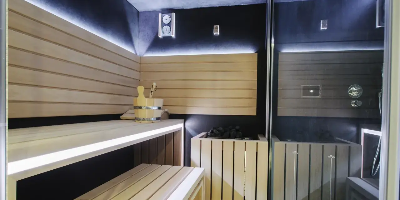 Nowoczesna sauna w domu z drewnianymi ławami, kamiennym piecem i dyskretnym oświetleniem LED. Idealne miejsce na relaks.
