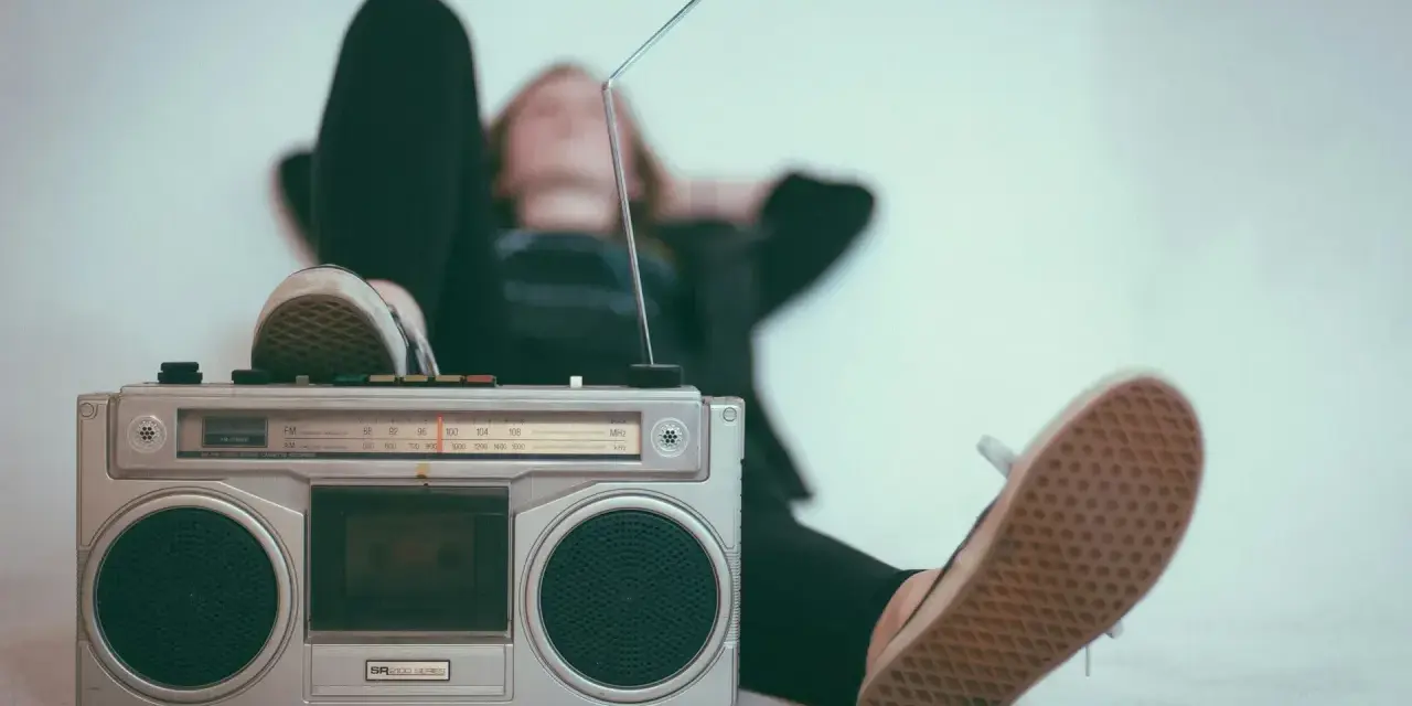 Osoba leży z nogami opartymi o boombox, słuchając muzyki. Idealny sposób, by sprawdzić, jak głośno można słuchać muzyki w dzień.