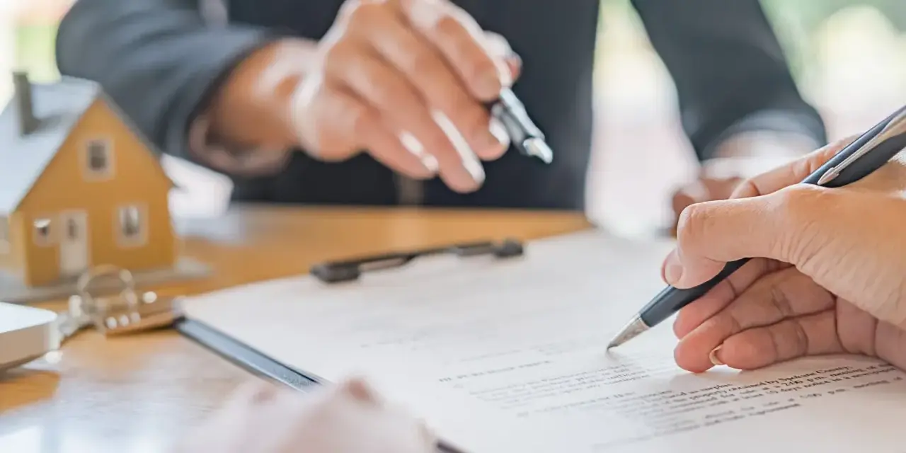 Podpisanie umowy najmu. Dwie osoby przy stole, jedna wskazuje na dokument, druga podpisuje. Obok model domu i klucze. Kiedy wypowiedzenie umowy najmu jest bezskuteczne.