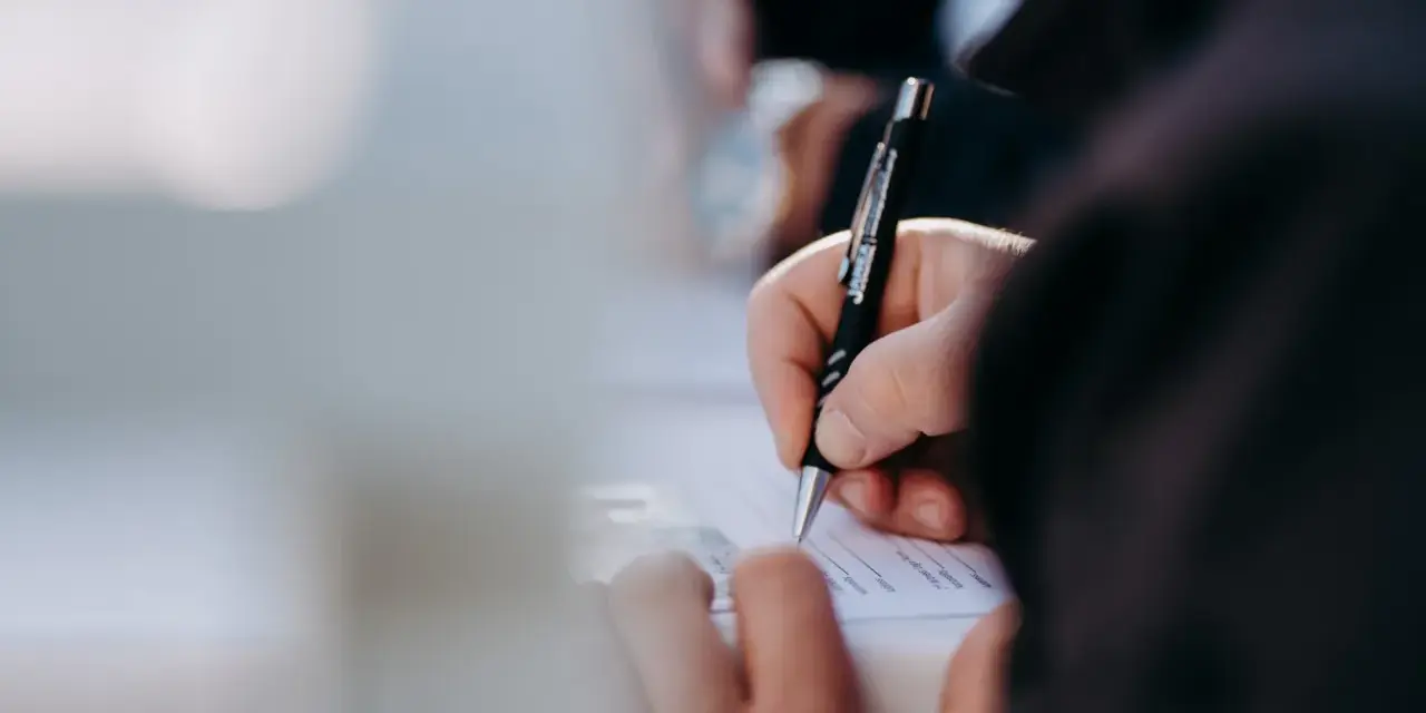 Dłoń pisze długopisem na dokumencie. Kto może zameldować osobę w domu? Właściwa osoba wypełnia formularz.