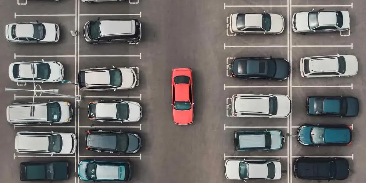 Widok z góry na parking, gdzie samochody są zaparkowane w strefie zamieszkania. W centrum wyróżnia się czerwony samochód.
