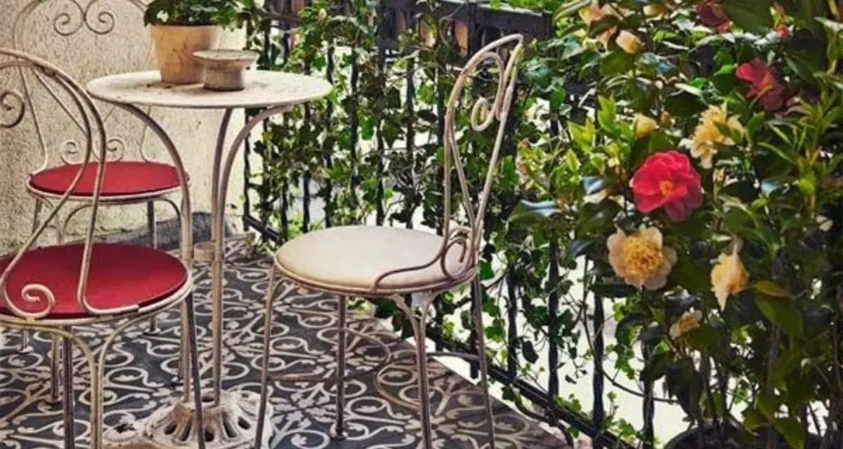 Uroczy balkon w stylu włoskim z metalowymi meblami, kwitnącymi kameliami i bluszczem. Idealne miejsce na poranną kawę.