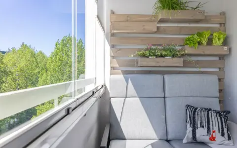 Przytulny balkon z szarą sofą, poduszką z liskiem i zielenią. Idealne miejsce, by zastanowić się, co na balkon posadzić.