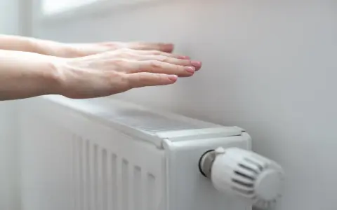 Dłonie ogrzewają się nad grzejnikiem, kiedy grzeją w blokach. Ciepło rozchodzi się po pokoju.