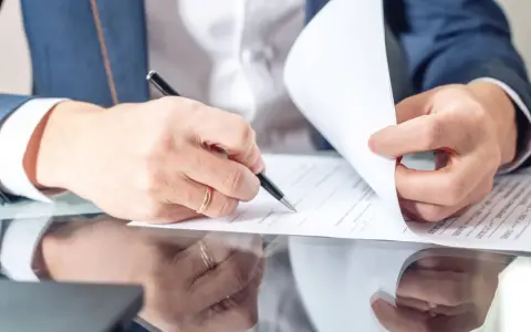 Mężczyzna w garniturze podpisuje dokumenty, co może oznaczać przedłużenie umowy najmu okazjonalnego.