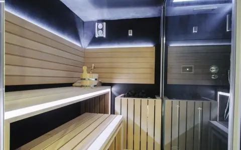 Nowoczesna sauna w domu z drewnianymi ławami, kamiennym piecem i dyskretnym oświetleniem LED. Idealne miejsce na relaks.