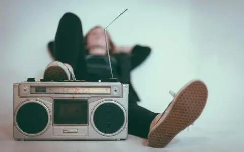 Osoba leży z nogami opartymi o boombox, słuchając muzyki. Idealny sposób, by sprawdzić, jak głośno można słuchać muzyki w dzień.
