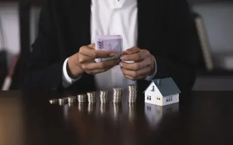 Osoba w garniturze liczy pieniądze obok modelu domu i stosów monet. Czy zaliczka jest zwrotna?