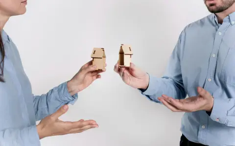 Dwie osoby trzymają miniaturowe domki, symbolizujące zniesienie współwłasności gdy współwłaściciel nie żyje.