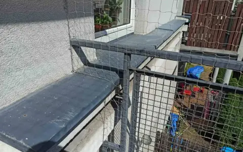 Siatkowanie balkonu cena: siatka zabezpiecza przed wypadnięciem, idealna dla kotów. Widok z góry na siatkę i balustradę.