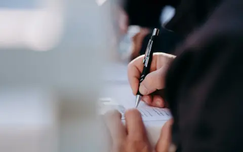 Dłoń pisze długopisem na dokumencie. Kto może zameldować osobę w domu? Właściwa osoba wypełnia formularz.