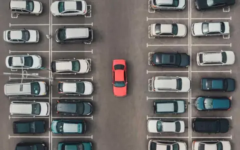 Widok z góry na parking, gdzie samochody są zaparkowane w strefie zamieszkania. W centrum wyróżnia się czerwony samochód.