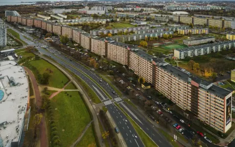 Najdłuższy blok w Polsce, falujący budynek mieszkalny z pomarańczową elewacją, otoczony zielenią i drogą z samochodami.