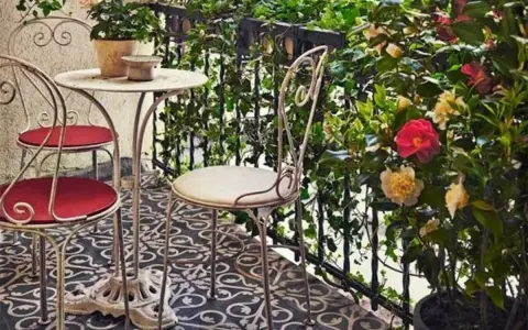 Uroczy balkon w stylu włoskim z metalowymi meblami, kwitnącymi kameliami i bluszczem. Idealne miejsce na poranną kawę.
