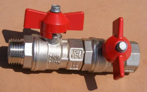 Metalowy zawór kulowy z czerwonymi rączkami, kluczowy element instalacji wodnej, stanowiący główny zawór wody w mieszkaniu.