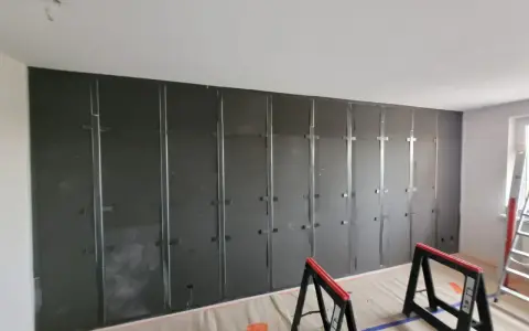 Montaż paneli wygłuszających ścianę od sąsiada. Metalowy stelaż i ciemne płyty tworzą barierę akustyczną.