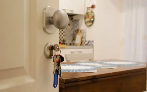 Klucze do mieszkania wiszą przy drzwiach. Czy zakup mieszkania można wrzucić w koszty? W tle kuchnia i stół.