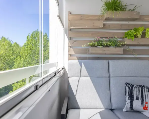 Przytulny balkon z szarą sofą, poduszką z liskiem i zielenią. Idealne miejsce, by zastanowić się, co na balkon posadzić.