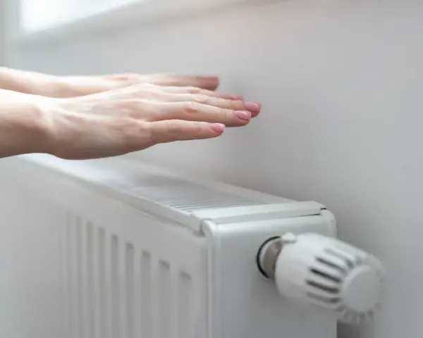 Dłonie ogrzewają się nad grzejnikiem, kiedy grzeją w blokach. Ciepło rozchodzi się po pokoju.