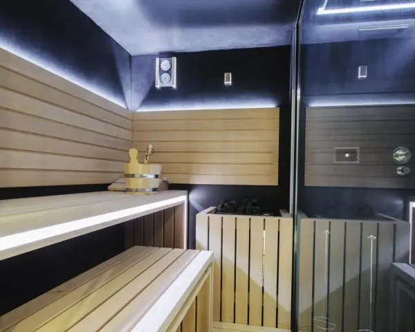 Nowoczesna sauna w domu z drewnianymi ławami, kamiennym piecem i dyskretnym oświetleniem LED. Idealne miejsce na relaks.
