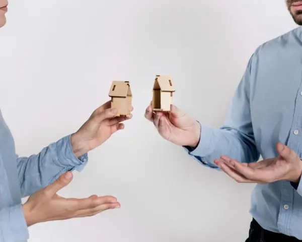 Dwie osoby trzymają miniaturowe domki, symbolizujące zniesienie współwłasności gdy współwłaściciel nie żyje.