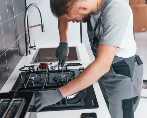 Fachowiec w rękawiczkach montuje podłączenie kuchenki gazowej w bloku. Narzędzia leżą obok.