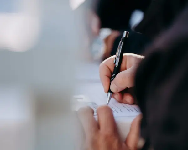 Dłoń pisze długopisem na dokumencie. Kto może zameldować osobę w domu? Właściwa osoba wypełnia formularz.