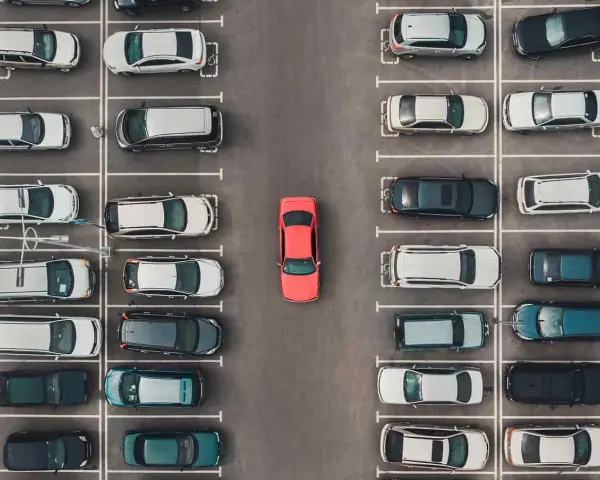 Widok z góry na parking, gdzie samochody są zaparkowane w strefie zamieszkania. W centrum wyróżnia się czerwony samochód.