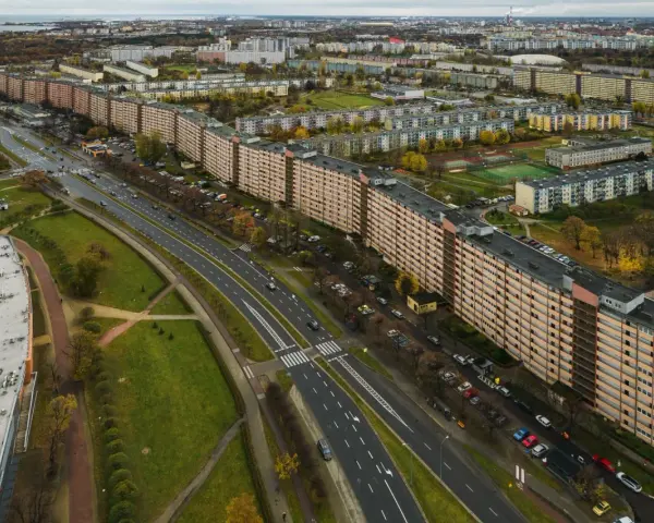 Najdłuższy blok w Polsce, falujący budynek mieszkalny z pomarańczową elewacją, otoczony zielenią i drogą z samochodami.