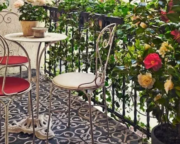 Uroczy balkon w stylu włoskim z metalowymi meblami, kwitnącymi kameliami i bluszczem. Idealne miejsce na poranną kawę.