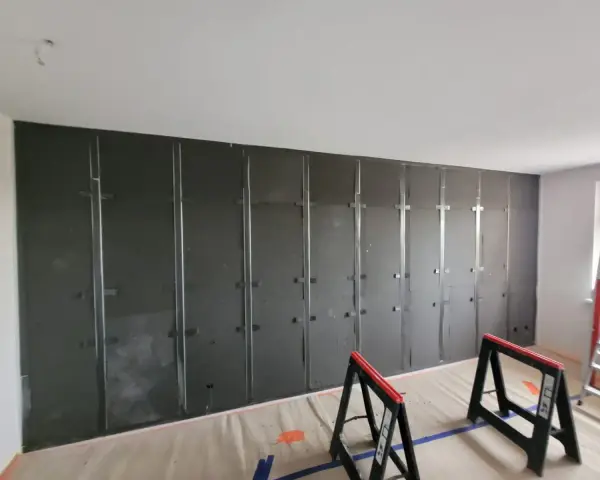 Montaż paneli wygłuszających ścianę od sąsiada. Metalowy stelaż i ciemne płyty tworzą barierę akustyczną.